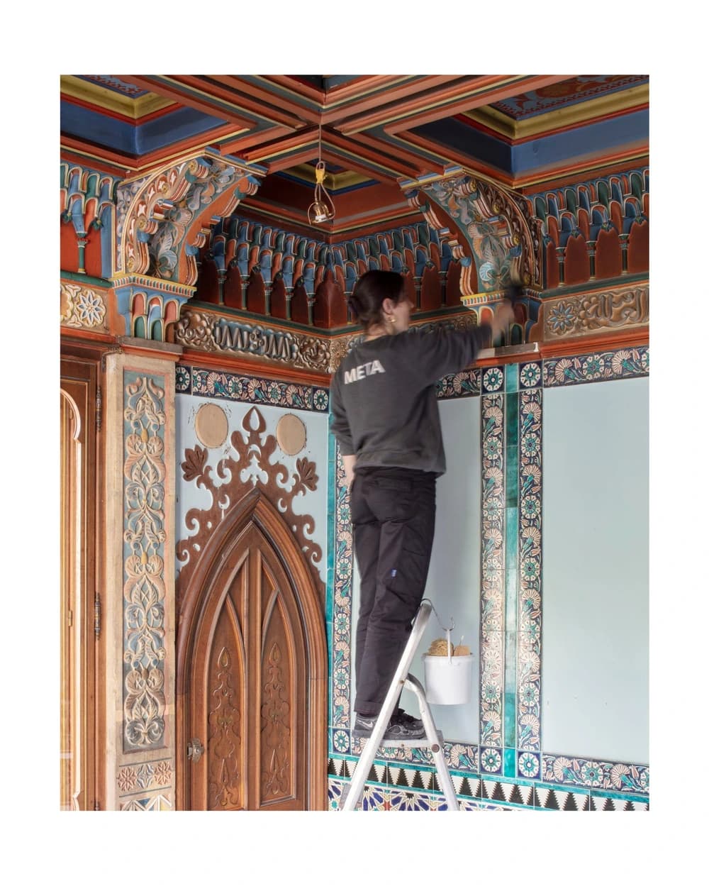 Une conservatrice-restauratrice intervient sur le décor architectural polychrome d’un salon du XIXe siècle.